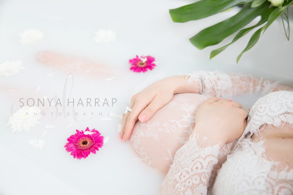 milk bath Pregnant mum in long lace maternity dress posing for maternity photoshoot by Sonya Harrap Photography in Welwyn Hertfordshire close up of baby bump with hands on