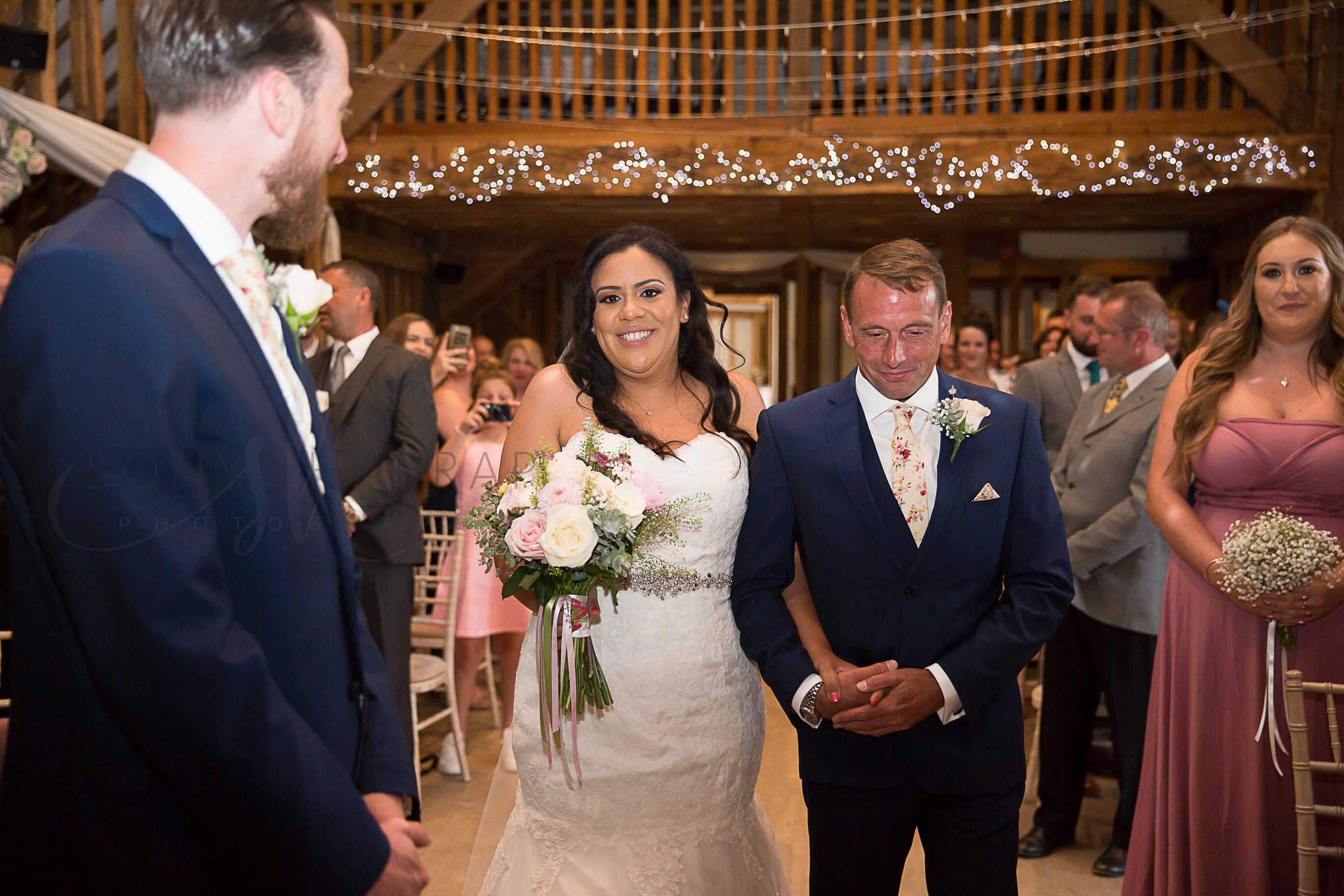 walking down the aisle with father Tewinbury farm hotel outdoor wedding photograph of bride and groom by Sonya Harrap photographer