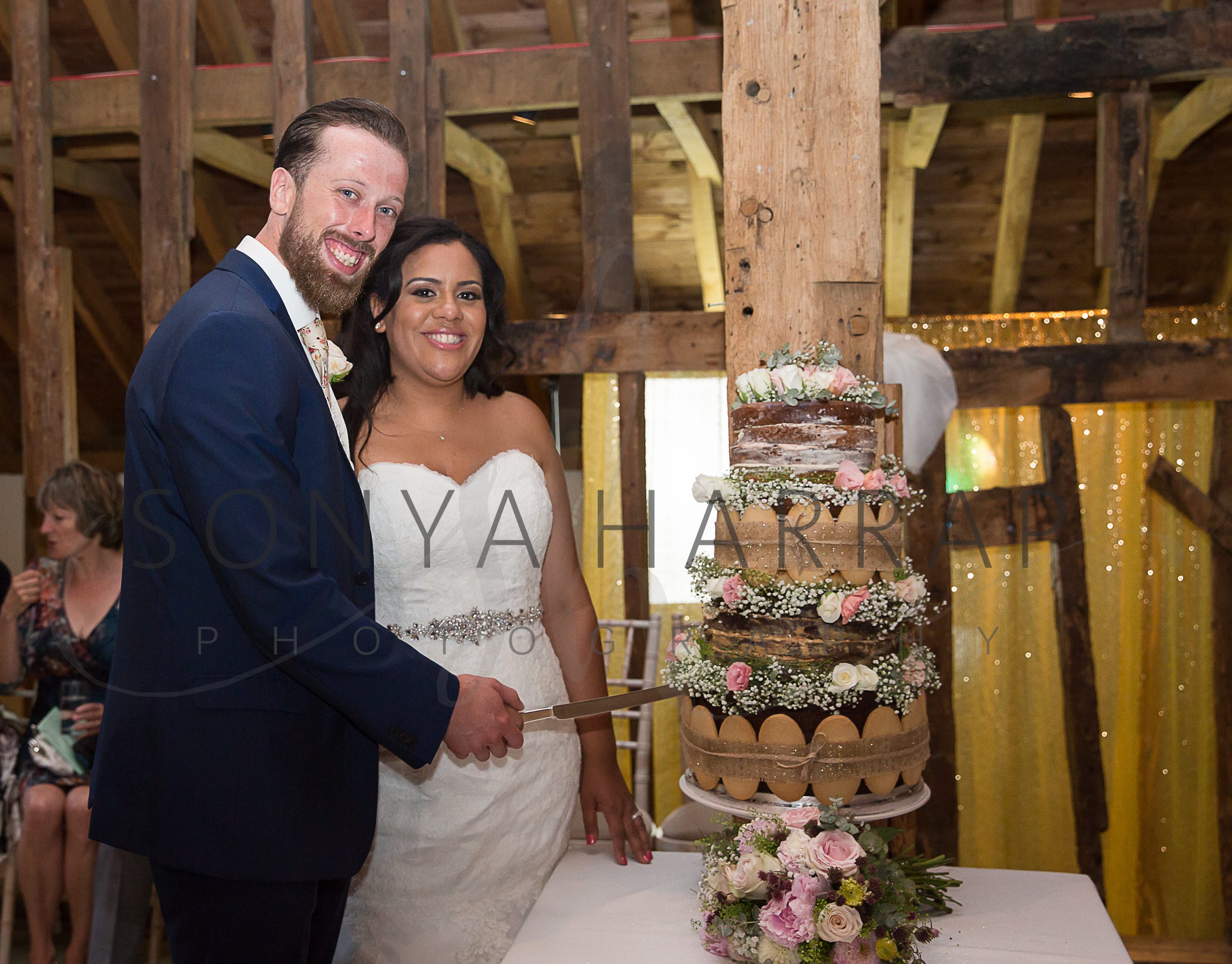 cake cutting in barn Tewinbury farm hotel wedding photograph of bride and groom by Sonya Harrap photographer