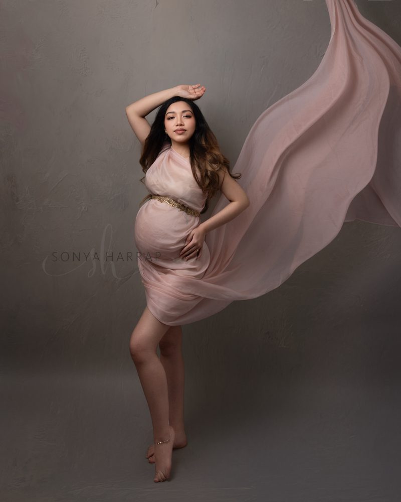 woman in baby pink at her maternity photoshoot in a studio in Hertfordshire welwyn garden city holding and showing her baby bump
