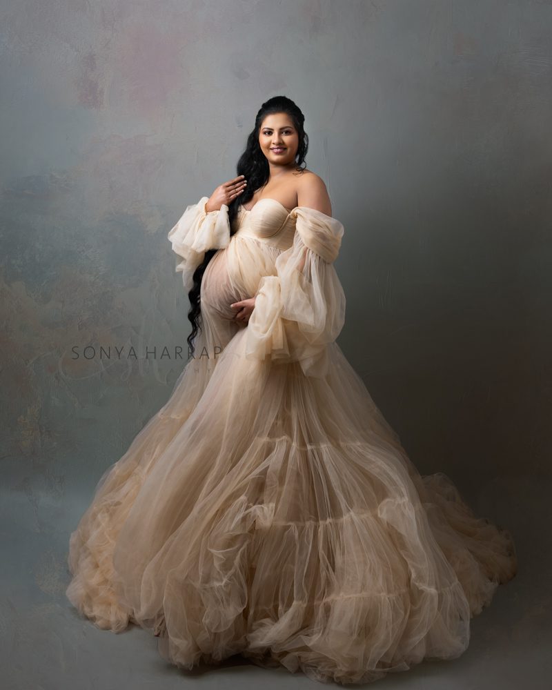 Indian women in studio Maternity photoshoot - wearing a big dress in ivory holding her baby bump by Sonya Harrap north London Hertfordshire, st albans, welwyn garden bishops stortford