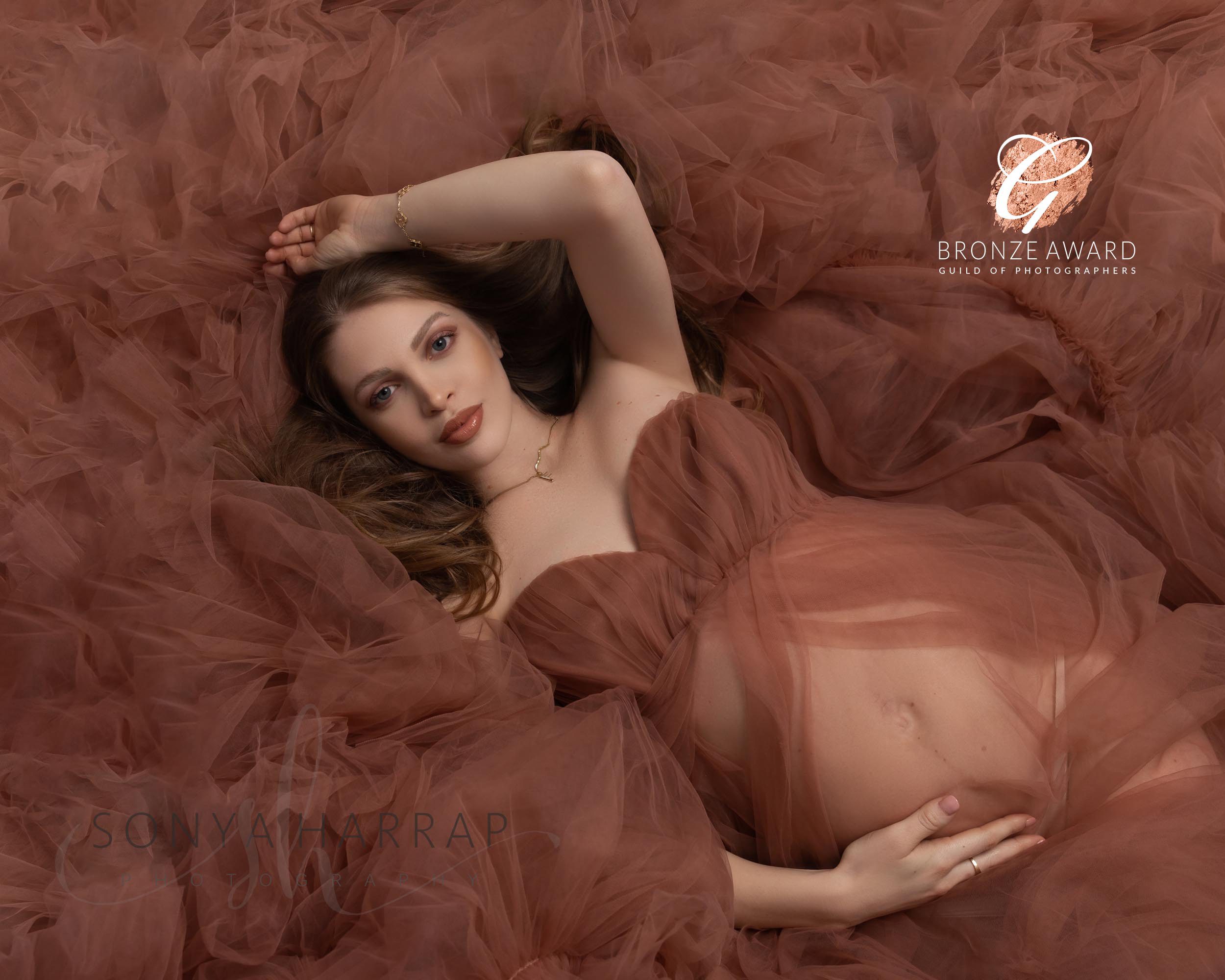 Pregnant woman in a brown flowing dress lying on the groud in a maternity photoshoot in Hertfordshire