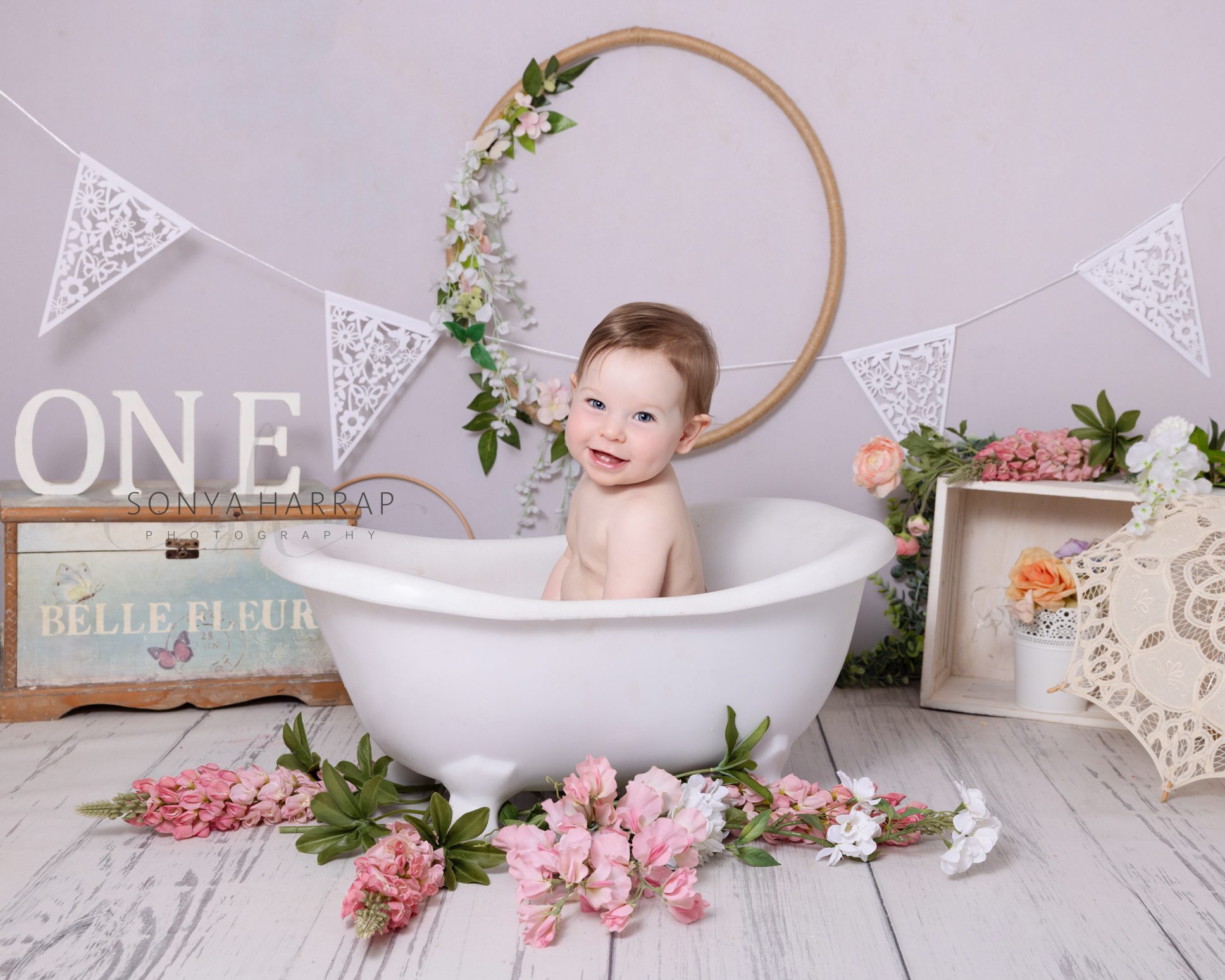 Baby splashing happily in a miniature roll-top bath after their cake smash session.