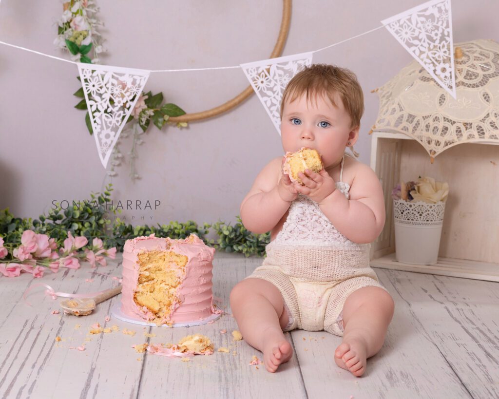 one year old girl with a cake in her hands at her first birthday cake smash photoshoot in Hertfordshire