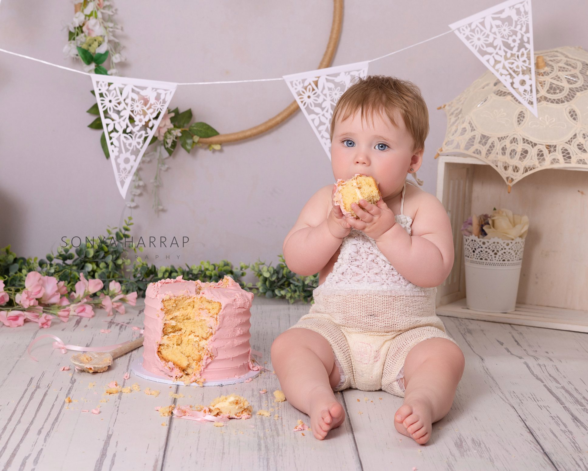 one year old girl with a cake in her hands at her first birthday cake smash photoshoot in Hertfordshire