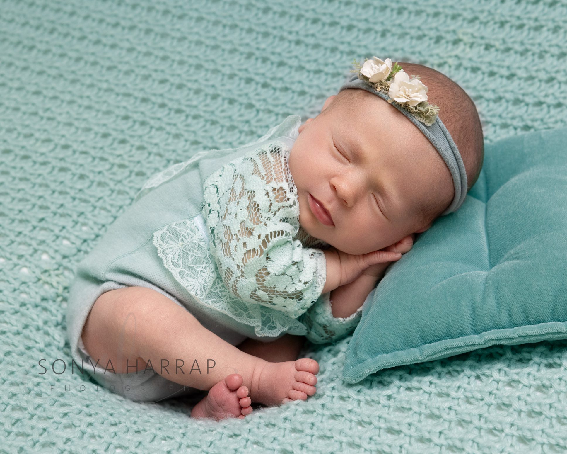 Sleeping newborn baby wrapped in soft pastel green fabrics during a newborn photography session in Hertfordshire.
